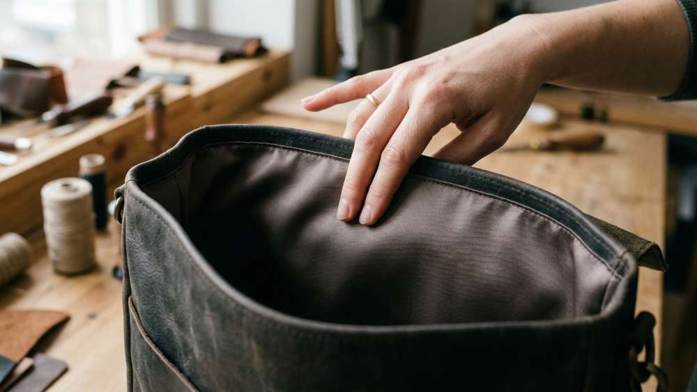Nærbilde av en hånd som kjenner på det glatte og blå fôrstoffet på innsiden av en veske for å vise komfort og profesjonell finish.